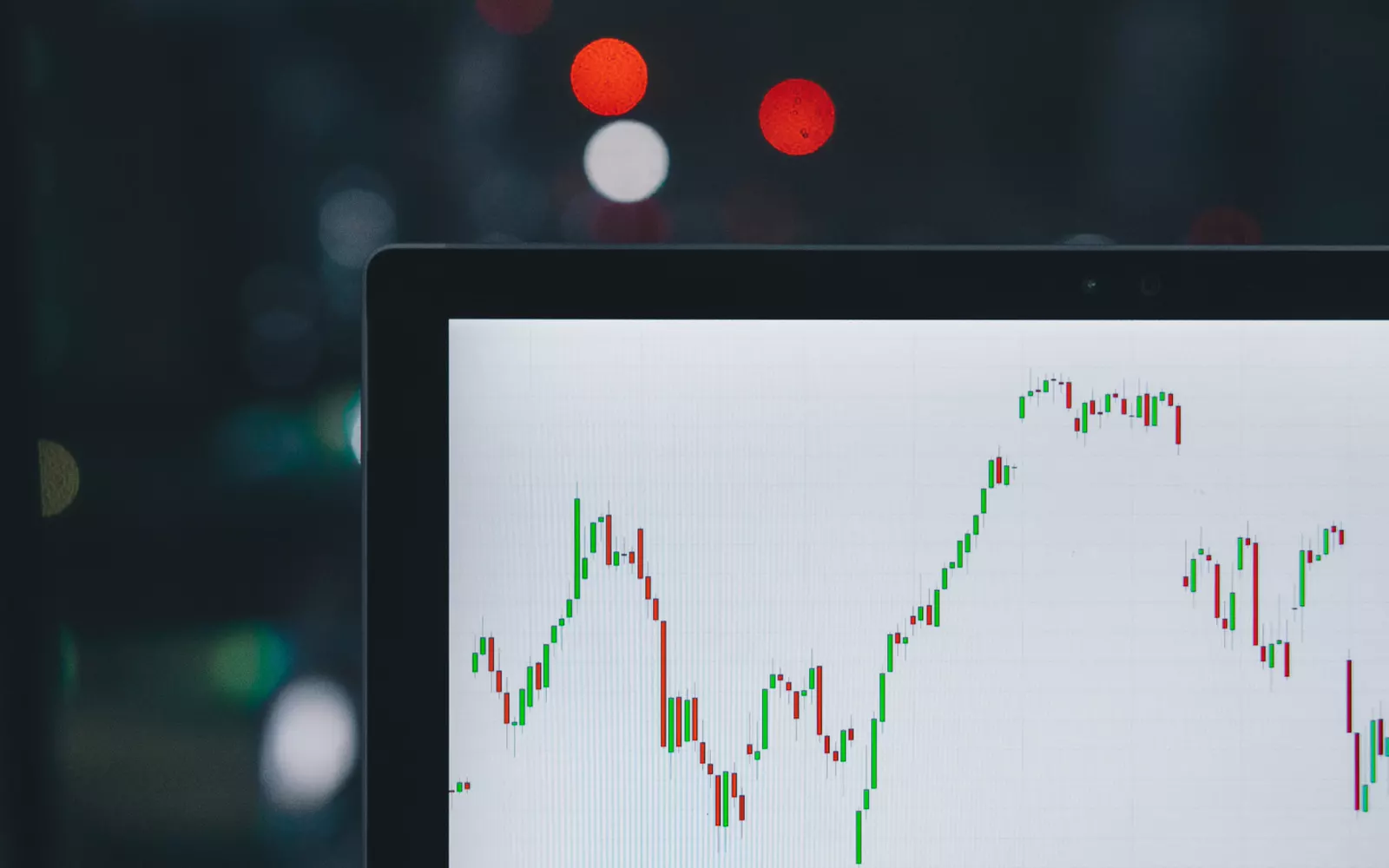 Candlestick trading chart on a laptop screen against dark, blurred city lights